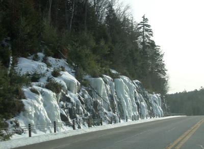 [Large chunks of ice that once ran down the tree-topped hillside on the left side of the road.]